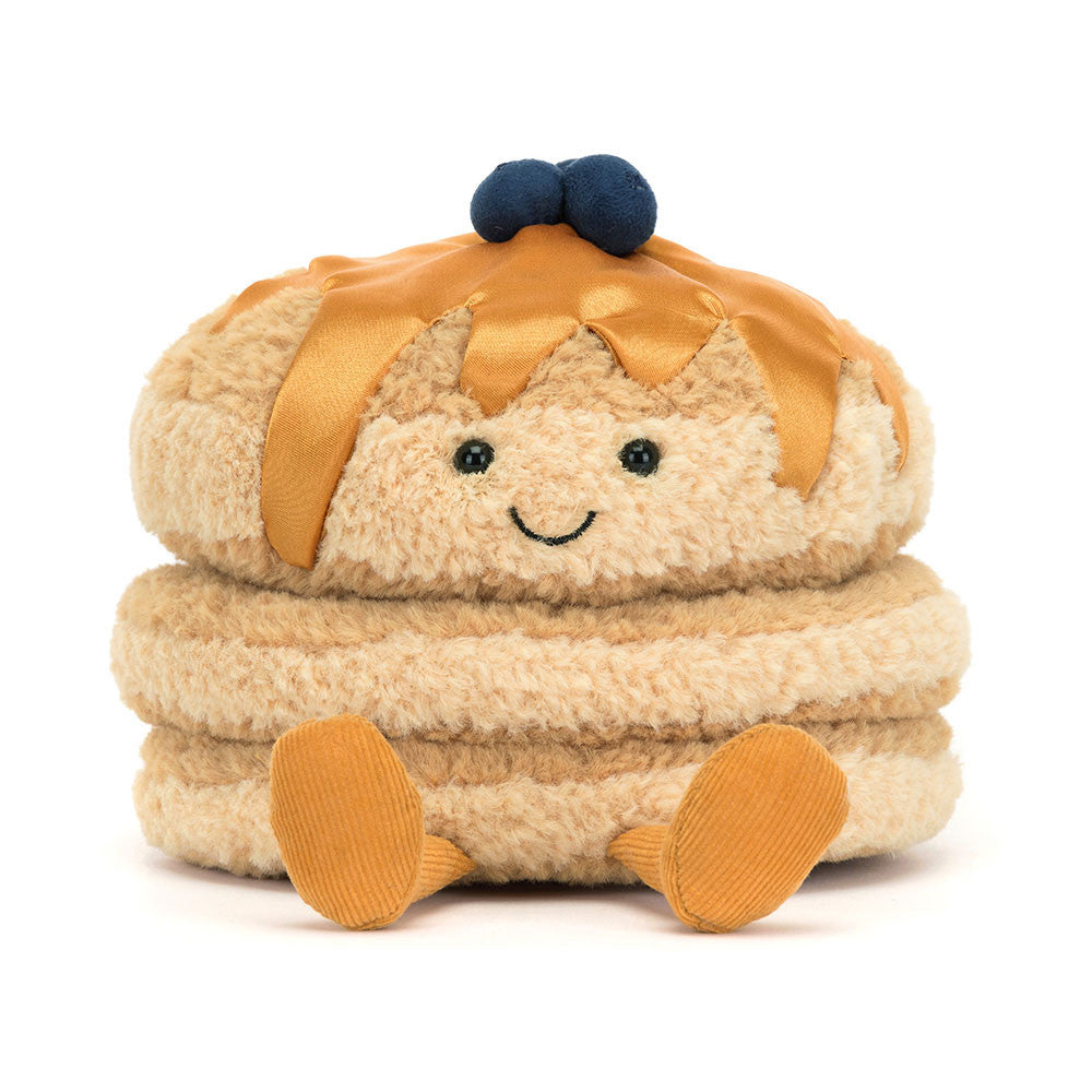 A front facing photo of a plush toy resembling a stack of pancakes with syrup and blueberries on top, with a smiling face and corduroy legs.