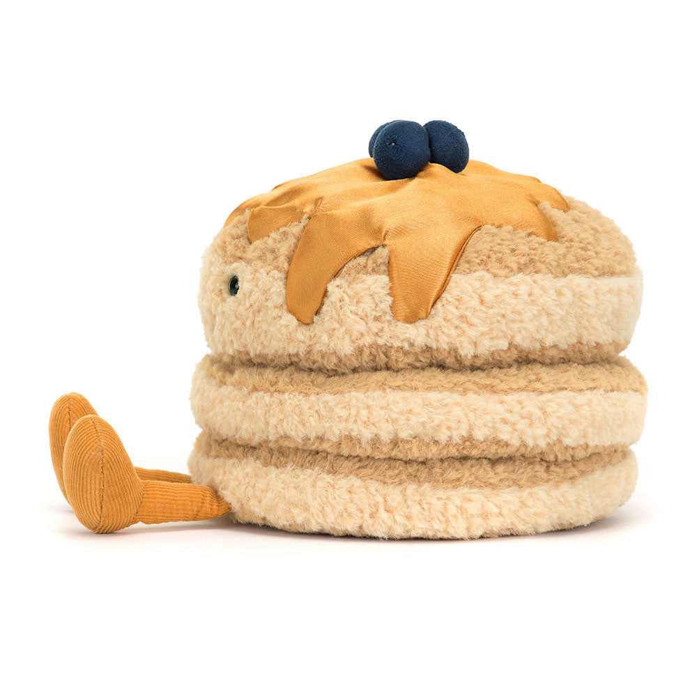 The side of a plush toy resembling a stack of pancakes with syrup and blueberries on top, with a smiling face and corduroy legs.