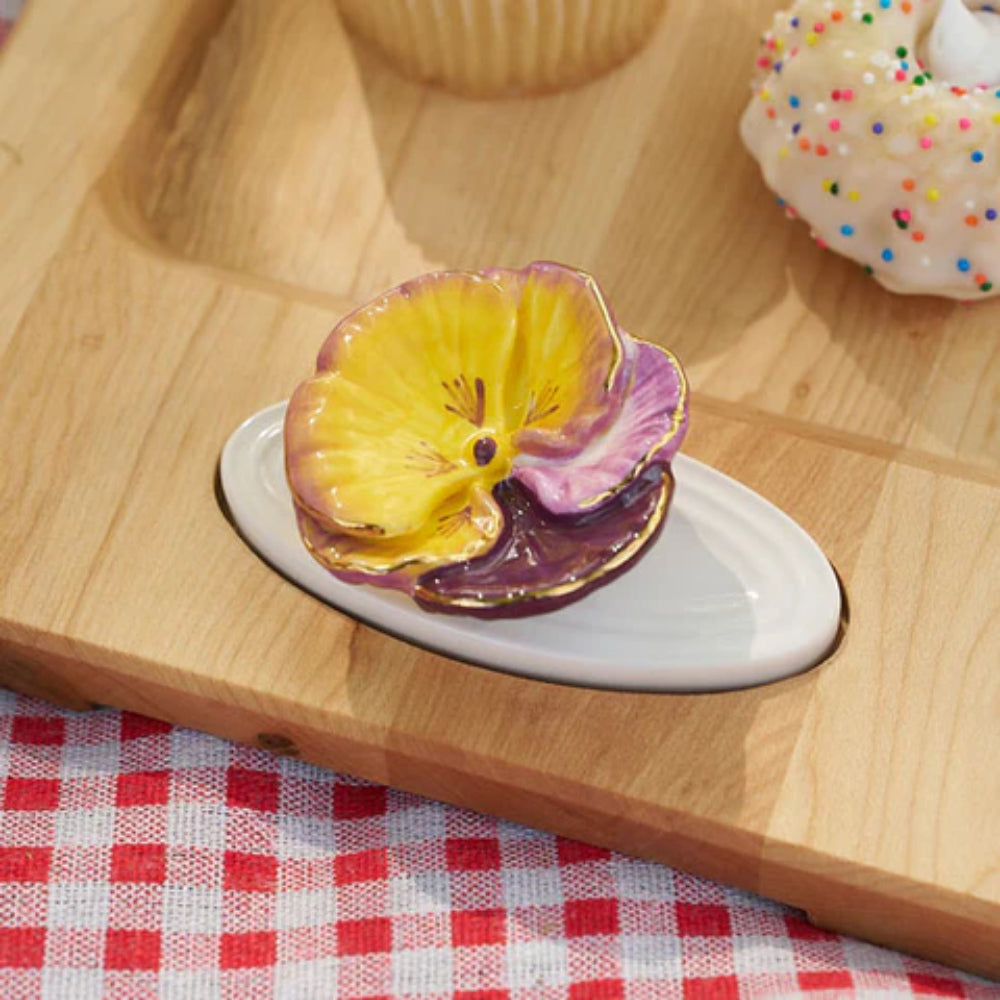 Colorful ceramic flower on a white plate with a wooden tray and red checkered tablecloth in the background.