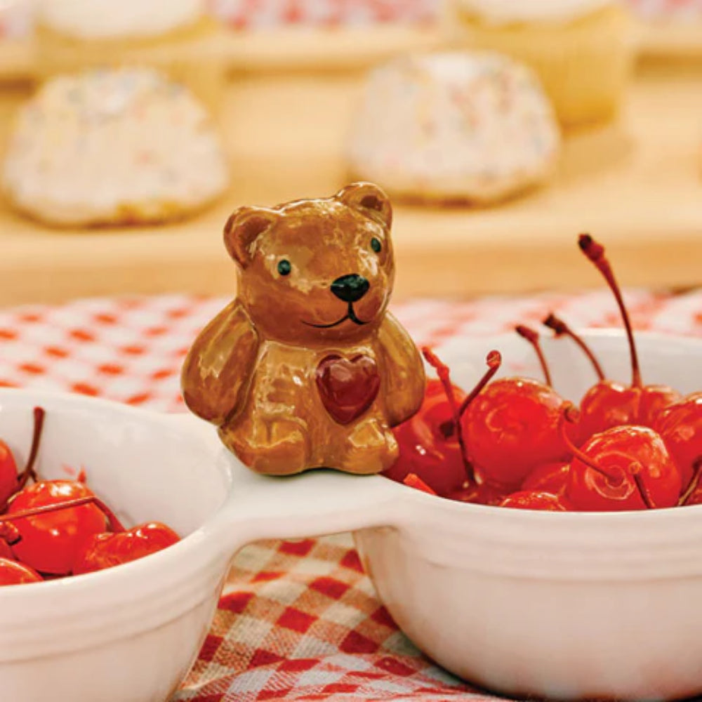 Brown bear figurine mini with a heart and cherries on a checkered tablecloth.