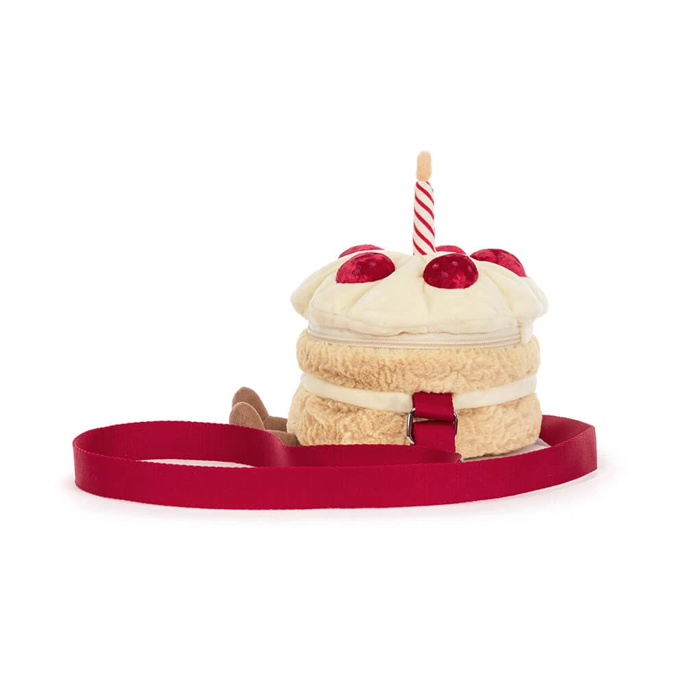 A plush cake-shaped bag with cream-colored frosting, red strawberry details, a striped candle, and a red strap, shown on a plain white background.