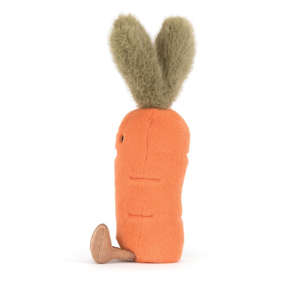 A side photo of a orange and green carrot plush toy with a smiling face on and brown legs a white background.