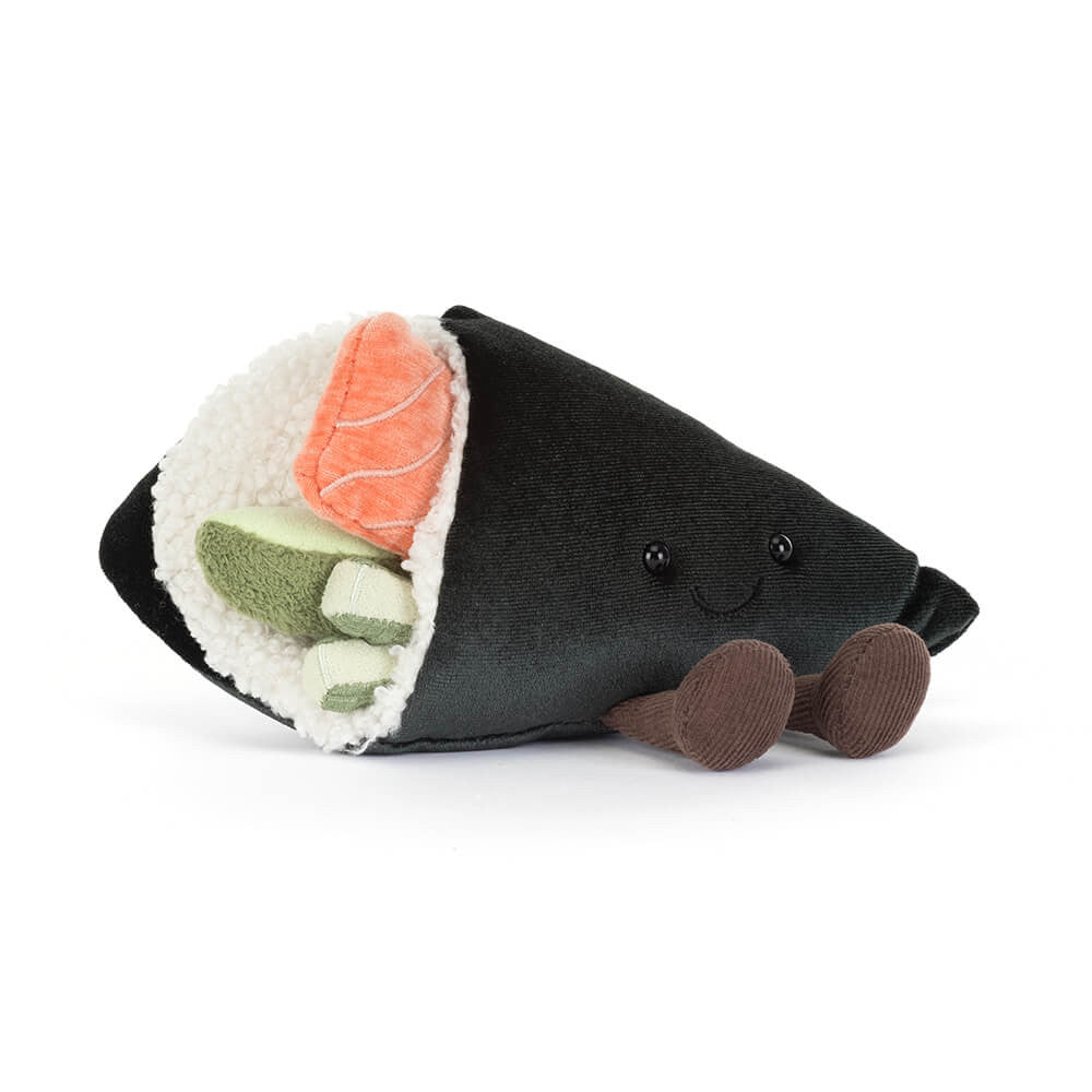 A side angled photo of a plush toy resembling a sushi roll with  rice, pink salmon, and green wasabi with a smiling face and brown legs on a white background.