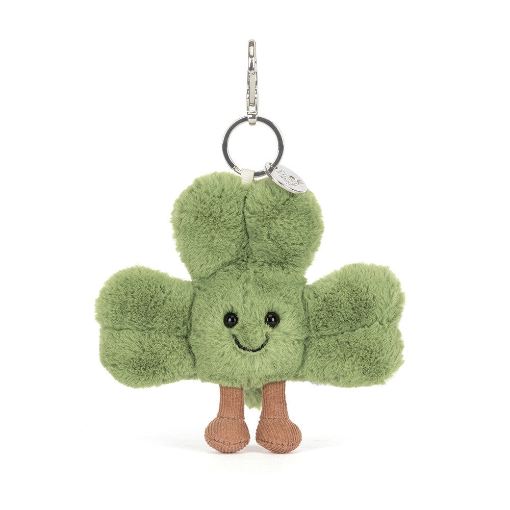An angled facing photo of a plush green  shamrock keychain with a smiling face on a white background