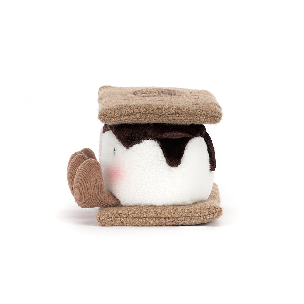 A side  photo of a plush toy resembling a s'more with brown gram cracker with pink and white marshmallows and chocolate on a white background.