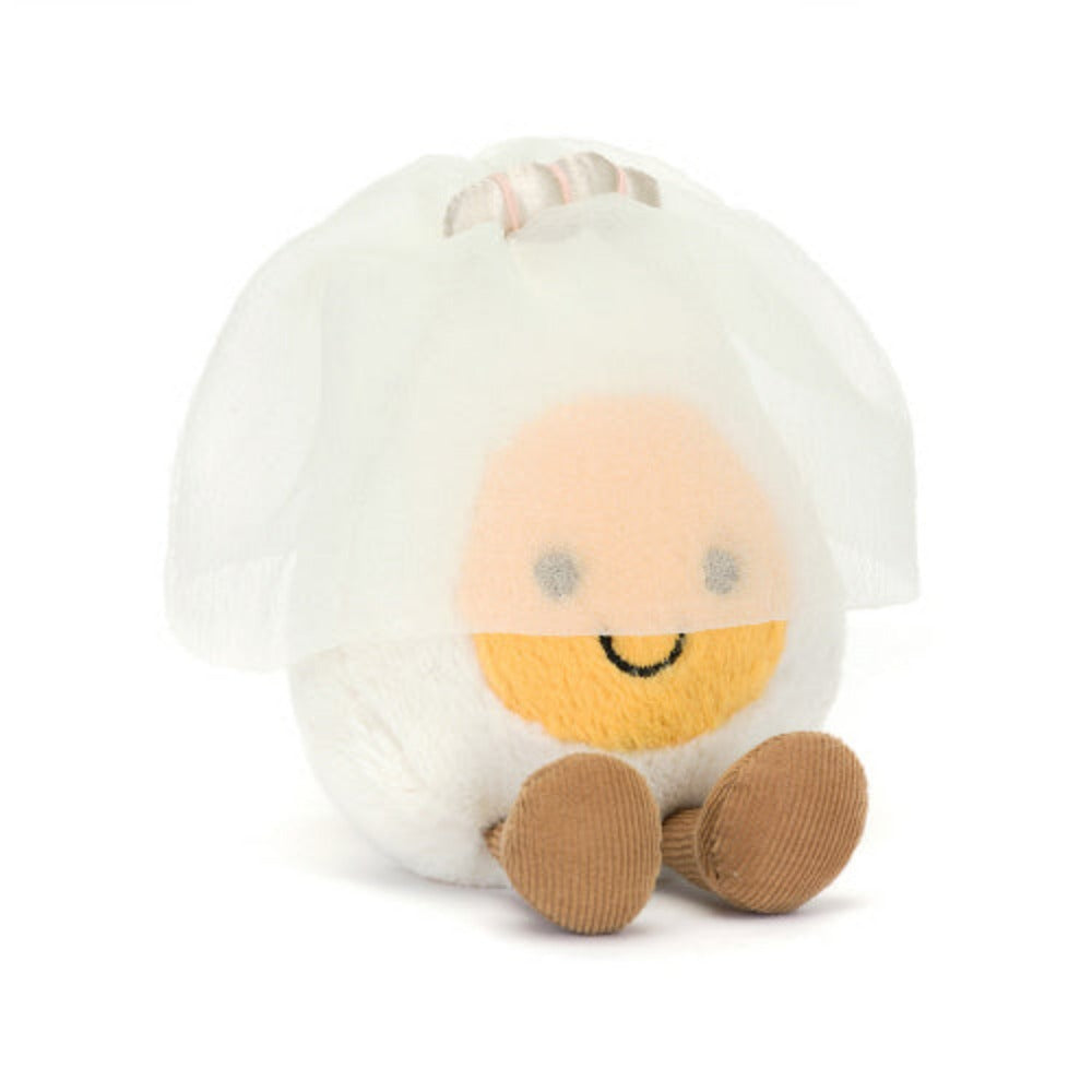 A angled photo of a plush toy representing a boiled egg dressed as a bride, with a white veil and a yellow face, sitting upright with cocoa cordy legs.