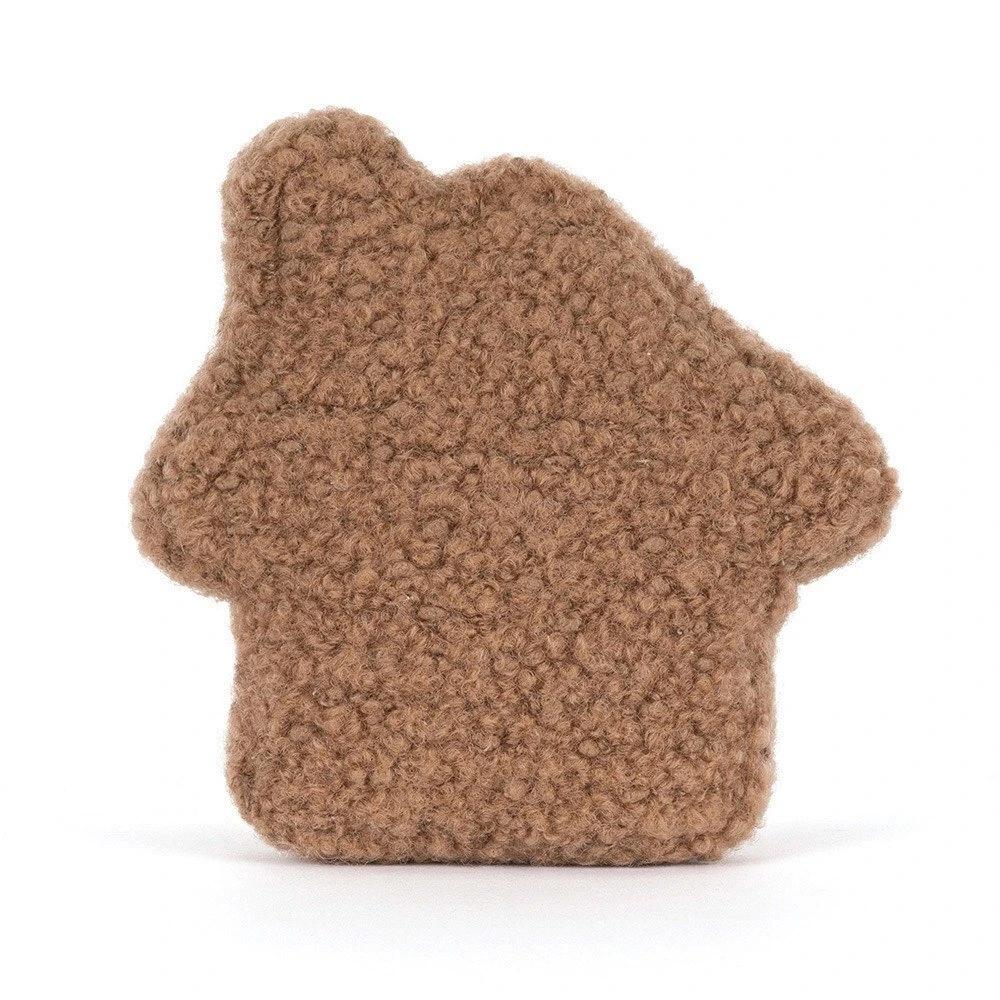 The back of a  plush gingerbread house plush toy with a brown curly-textured body, cream-colored icing details, embroidered facial features, and two small plush feet, photographed on a clean white background.