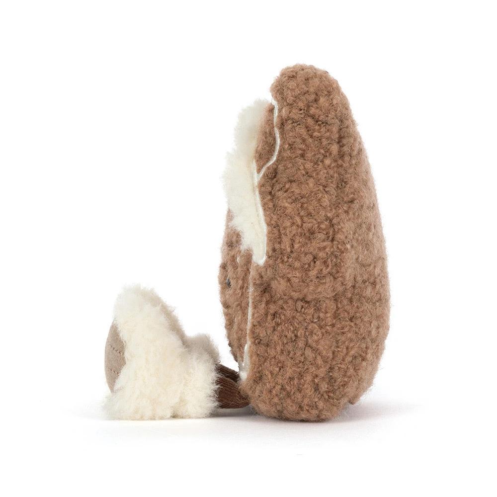 A side of a plush gingerbread house plush toy with a brown curly-textured body, cream-colored icing details, embroidered facial features, and two small plush feet, photographed on a clean white background.