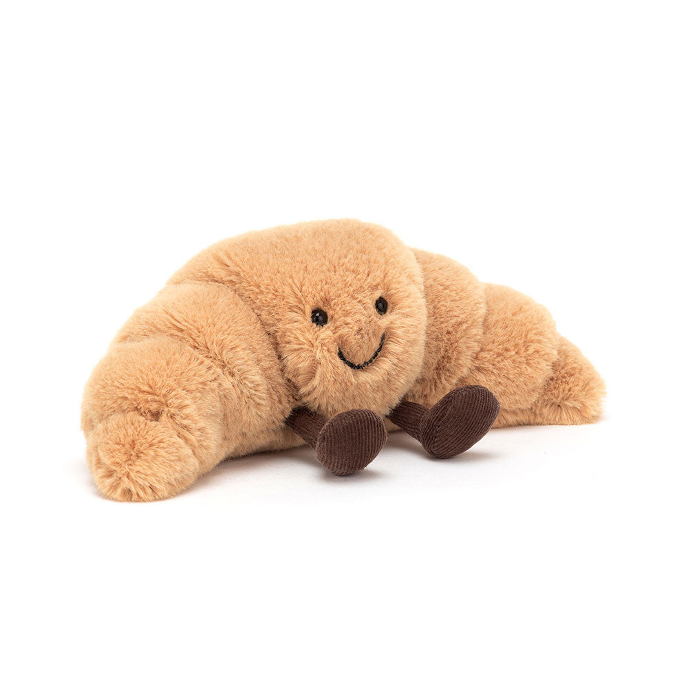 A small sized plush toy resembling a croissant with a happy facial expression and chocolate colored boots on a white backround.