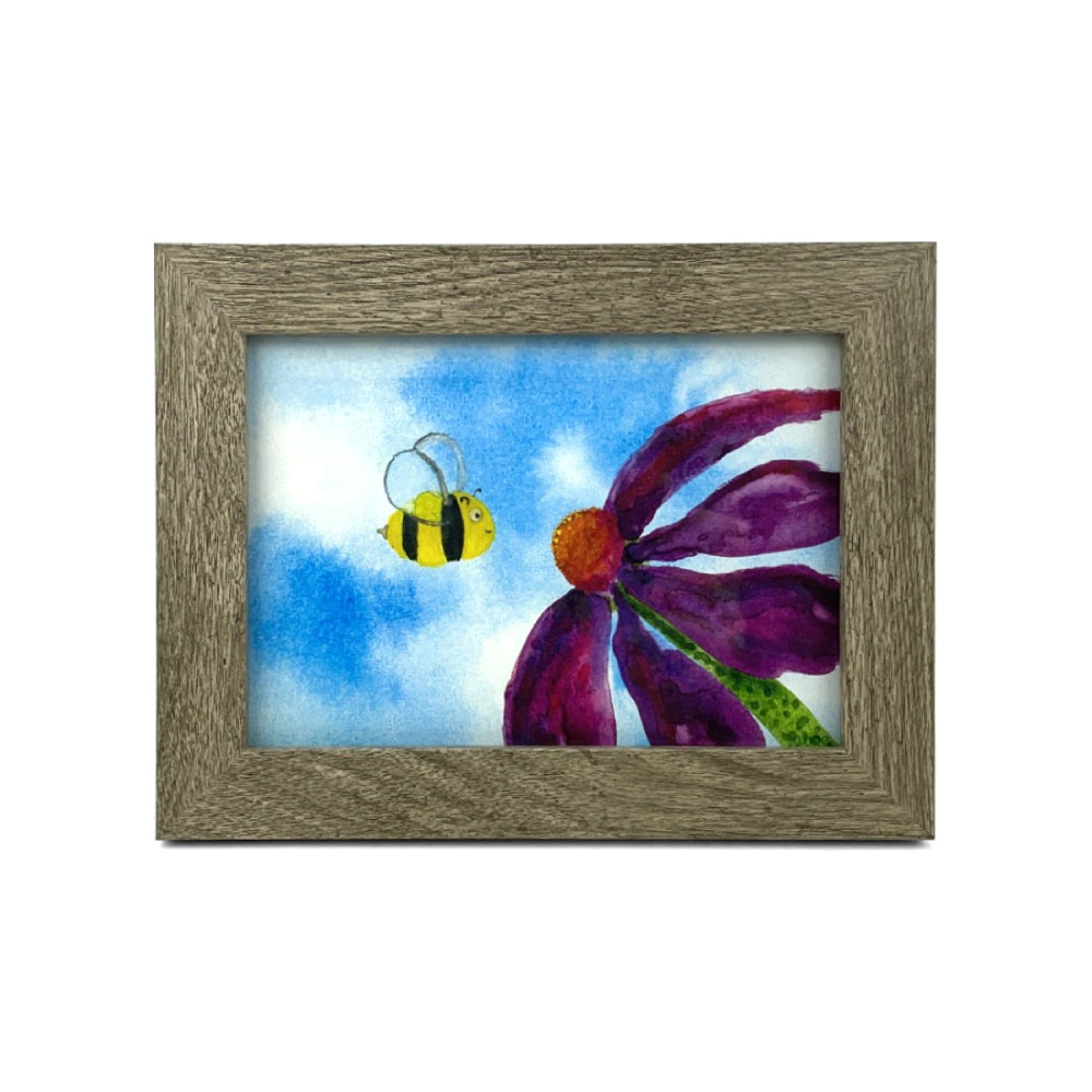 Framed artwork of a purple flower and a bee on a blue sky background on a white backround.