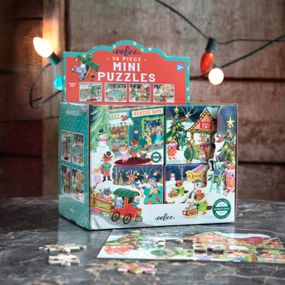 Box of eeBoo mini puzzles with a few pieces on a wooden surface, surrounded by Christmas lights.