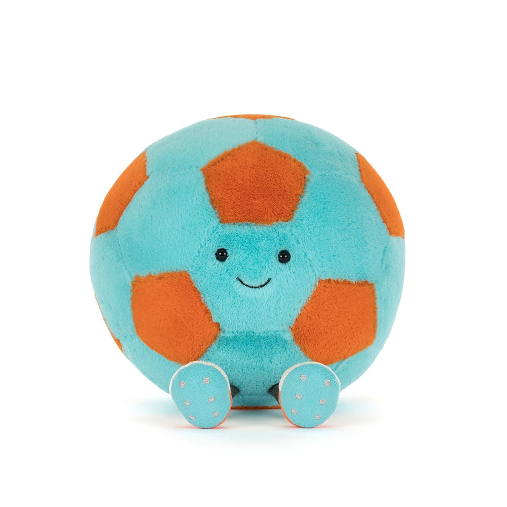 A photo of a teal and orange Jellycat Amuseables Soccer Ball push toy with a smiling face and white legs on a white background.