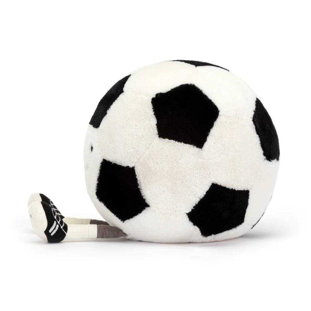 A side photo of a  plush toy resembling a white and black soccer ball, featuring a friendly face and legs on a white backround.