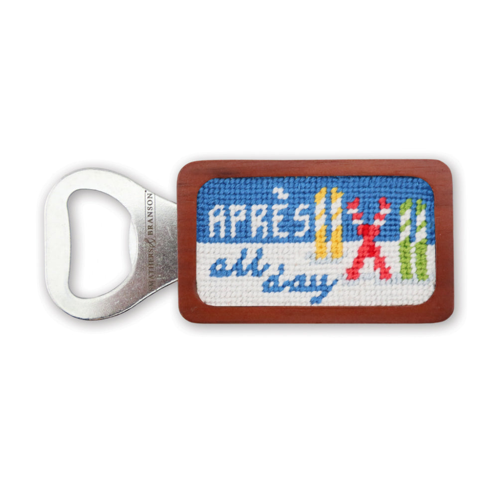 A wooden and metal bottle opener featuring a colorful cross-stitch style design with the French phrase 'Après all day' and small red, yellow, and green crossed skis, shown on a plain white background.