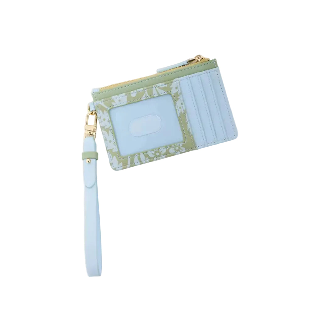 A light blue faux leather card holder and wristlet wallet with a green floral patterned trim, gold-tone zipper, and a matching light blue wrist strap, shown on a warm off-white background.