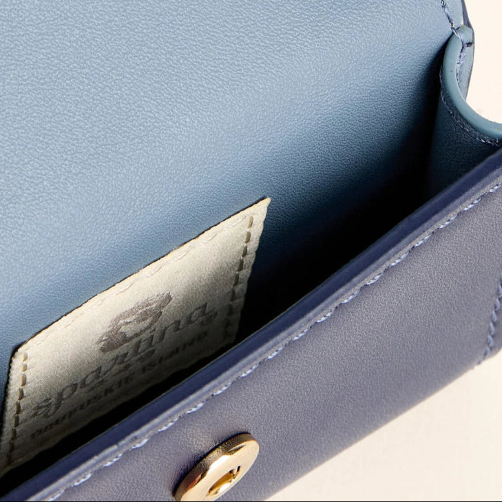 Close-up of a blue leather clutch or wallet showing the interior, a stitched interior pocket with a visible Spartina label, and a gold-tone snap button.