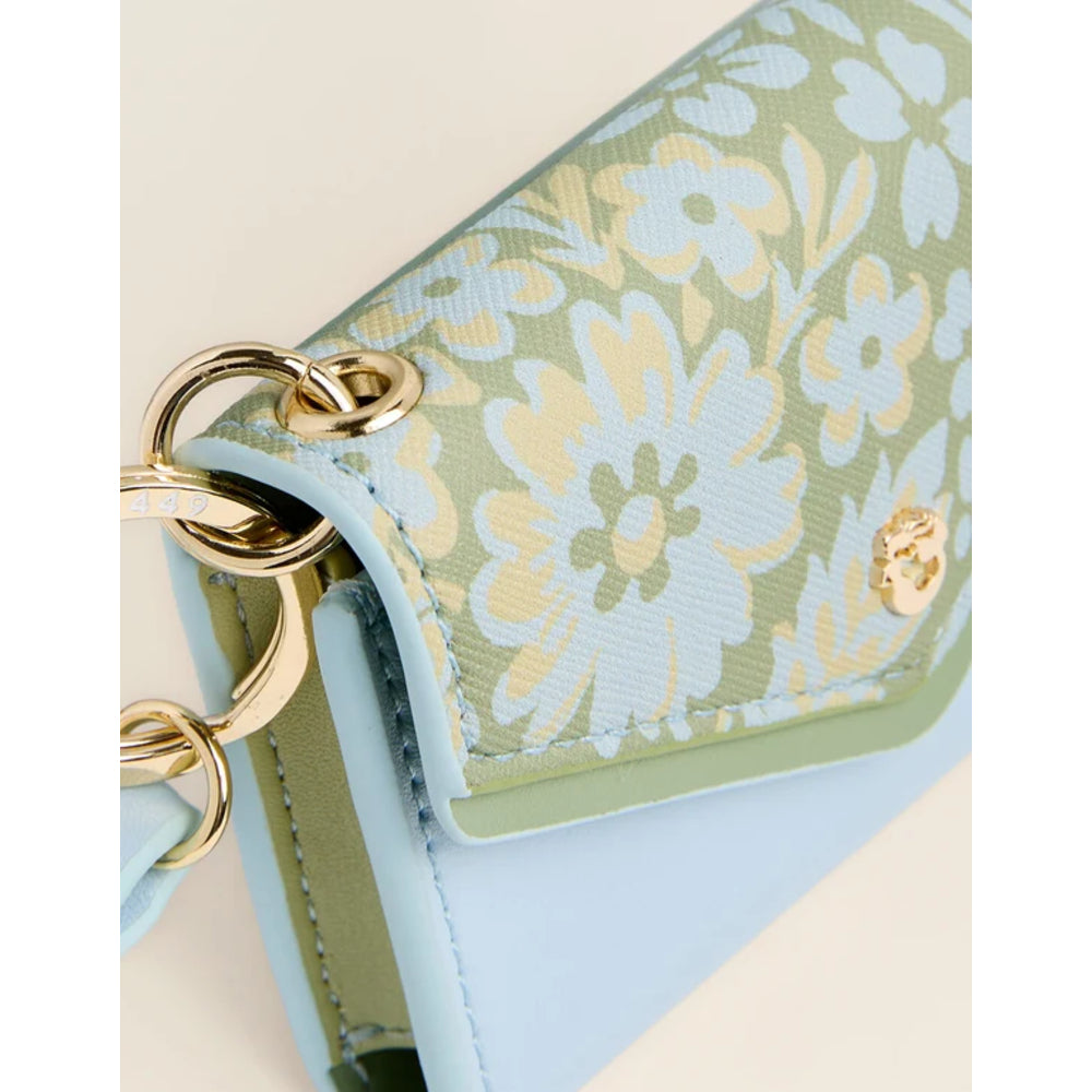 Close-up of a handbag flap in a sage green floral jacquard pattern with a light blue leather trim and gold-tone hardware.