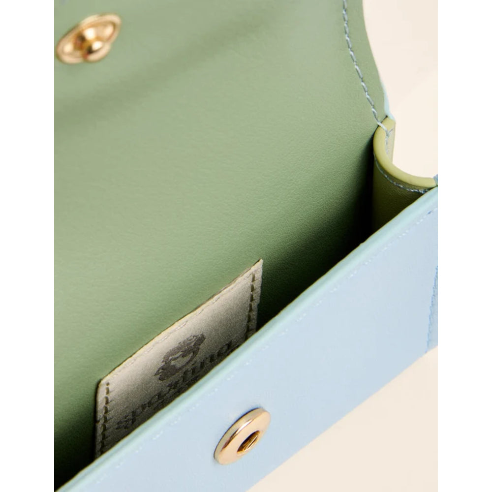 Close-up of a light blue and sage green leather clutch or wallet, showing the interior lining, gold-tone snap button, and a brand label.