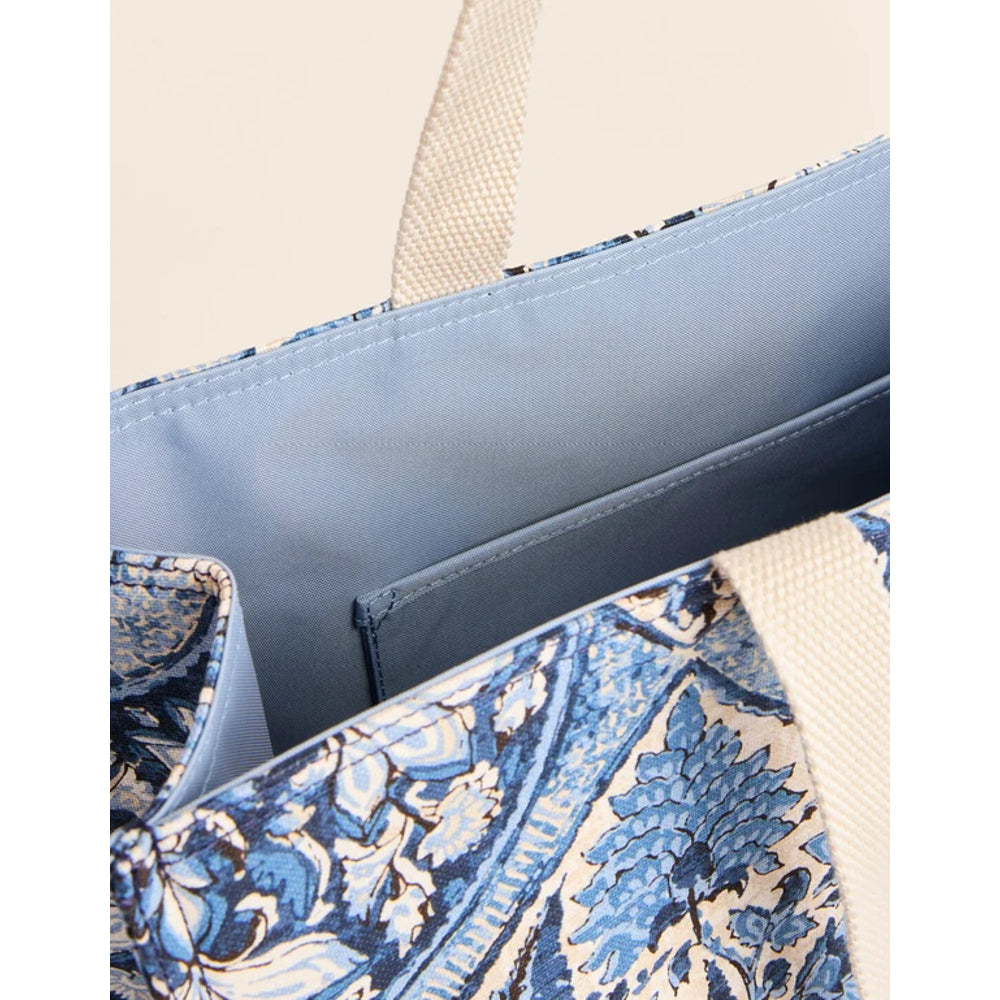 Close-up of a tote bag showing the interior with a light blue lining, a side pocket, and a blue and cream floral patterned fabric exterior with beige woven handles.