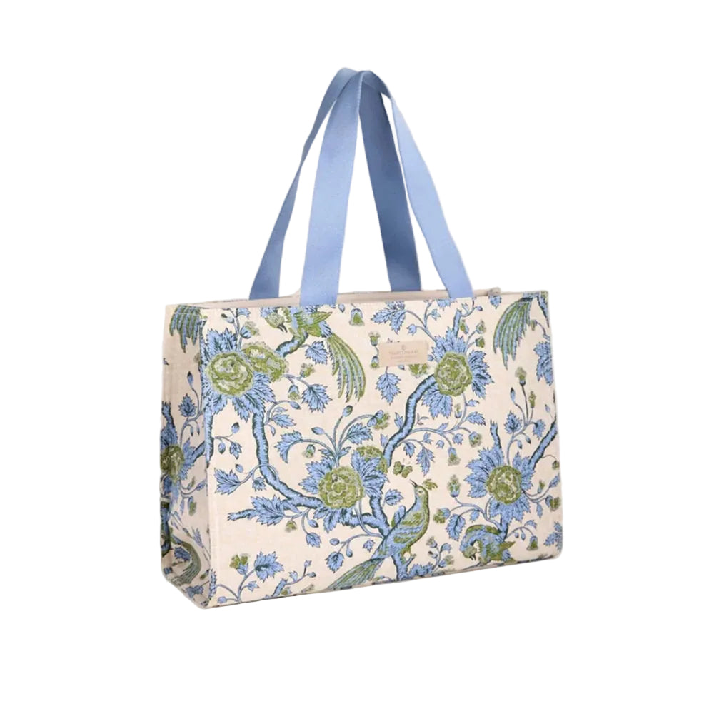 A tote bag with a blue and green floral peacock pattern on a cream background, featuring light blue fabric shoulder straps, photographed against a solid white background.