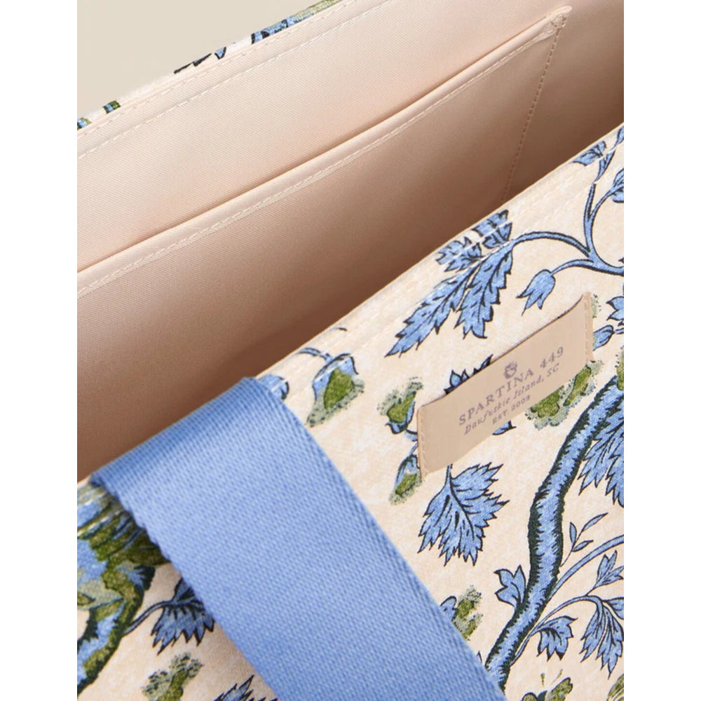 Close-up of a patterned fabric bag or clutch with a beige base, blue floral print, and a wide blue strap. A small leather brand patch reads SPARTINA 449.