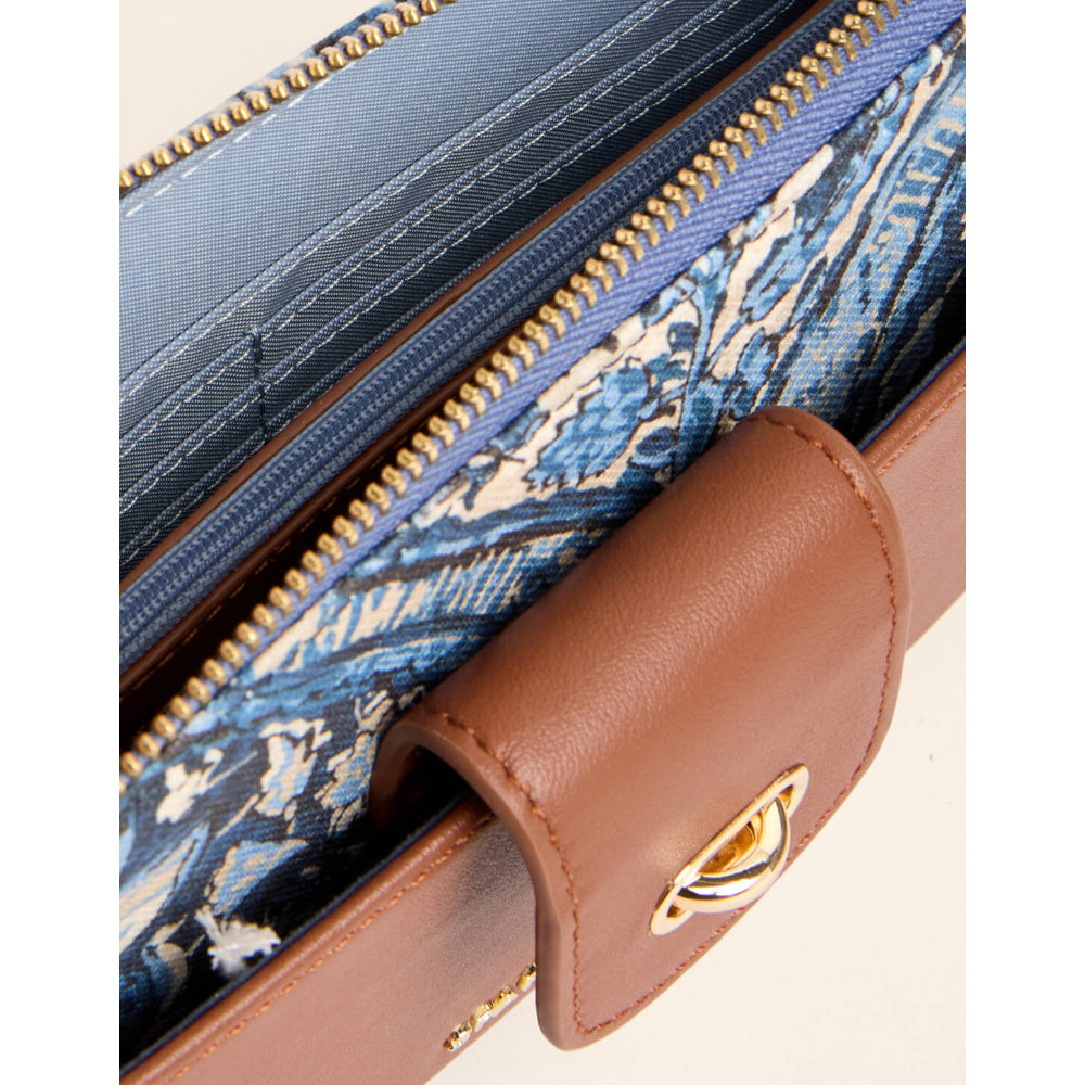 Close-up of a brown leather wallet or clutch showing a blue and white patterned fabric interior, gold-tone zippers, and a gold clasp on a light beige background.