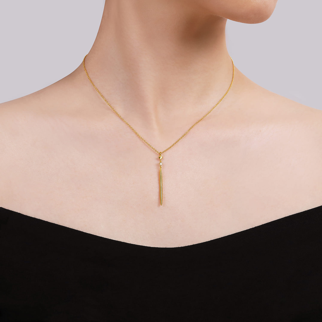 Gold necklace with a tassel pendant on a mannequin against a neutral background