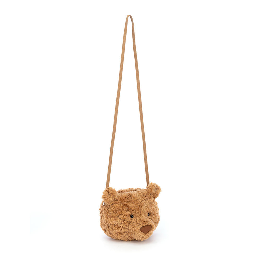 A  photo showing the full strap of a plush bear-shaped cross-body bag with a brown maple-syrup color, petal-fold ears, and a sturdy silver zipper. 