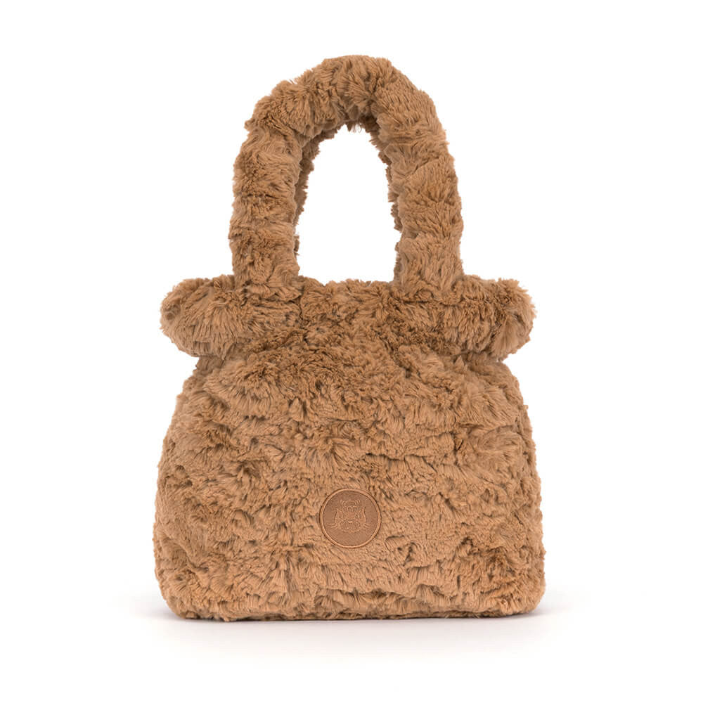 A small brown faux fur handbag with a top handle and a circular embossed logo patch on the front, photographed against a plain white background.