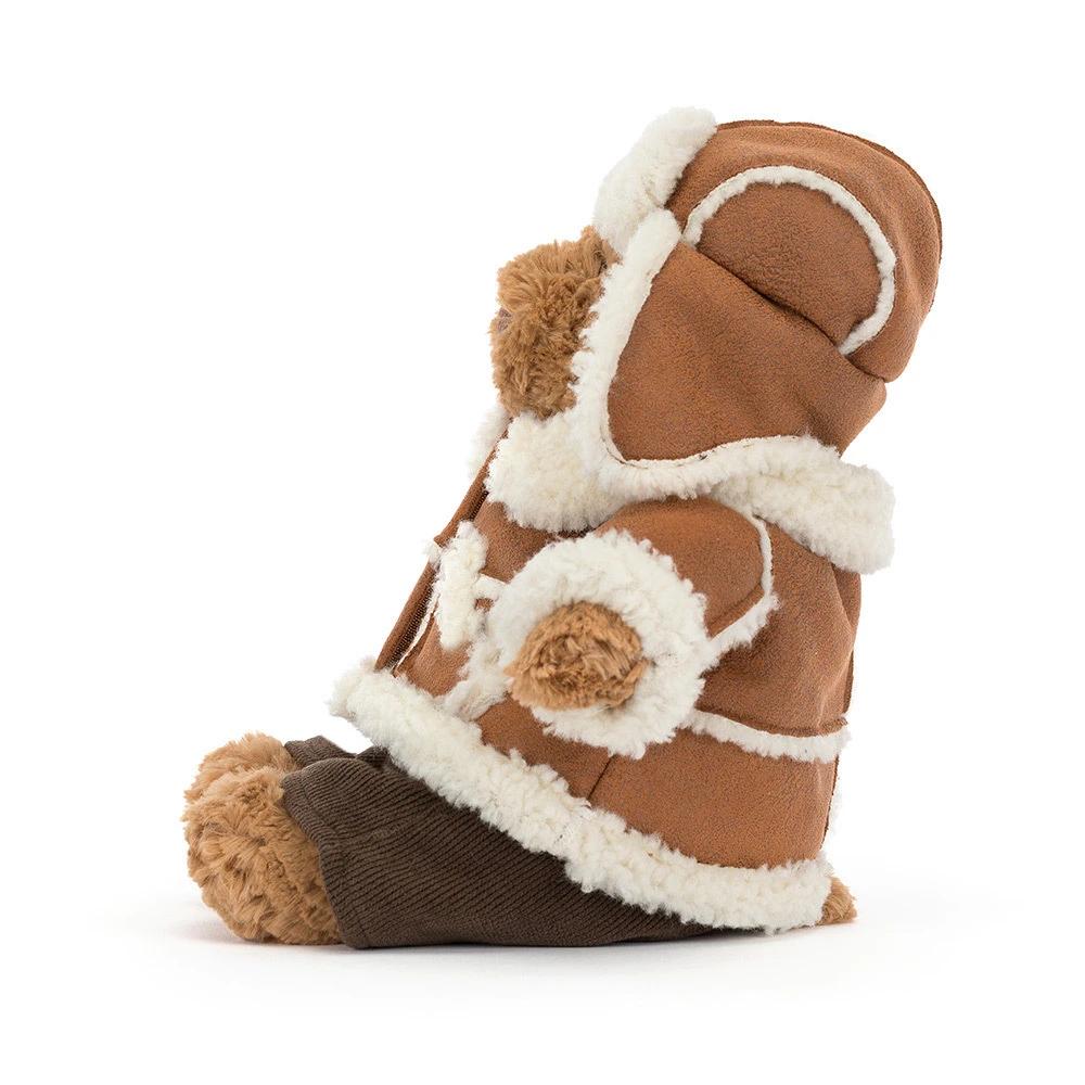 The side of a plush teddy bear dressed in a brown suede-like winter coat with cream sherpa lining and a dark brown bootie underneath, photographed on a clean white background.