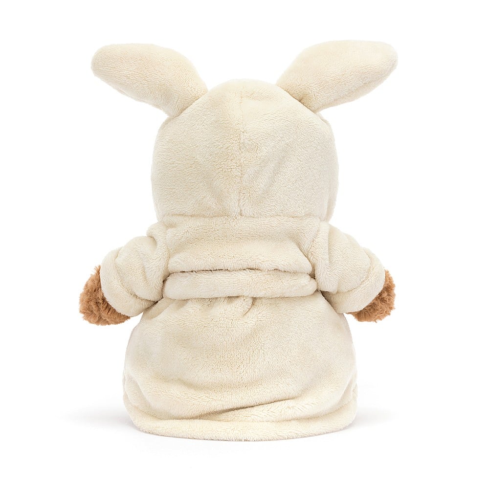 A side photo of the back of an stuffed teddy bear wearing a cream bath robe  robe with a hood and bunny ears on a white background.
