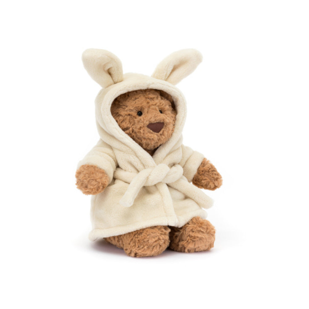 Stuffed teddy bear wearing a cream bath robe with a hood and bunny ears on a white background.