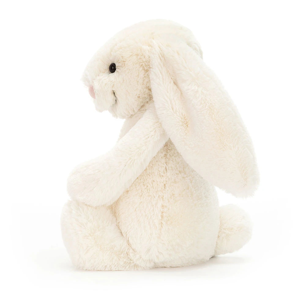 A side photo of a medium/original  sized cream-colored plush bunny toy on a white background.