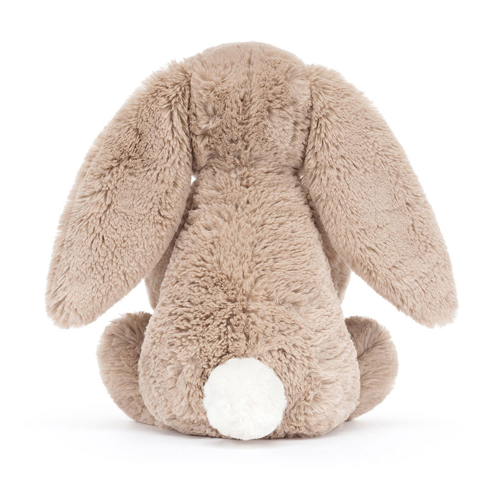 A photo of the back of a  beige plush toy bunny holding a cupcake with a candle on a white background.