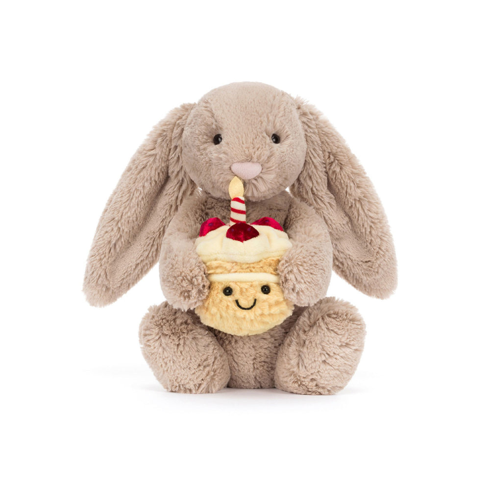 A beige plush toy bunny holding a cupcake with a candle on a white background.