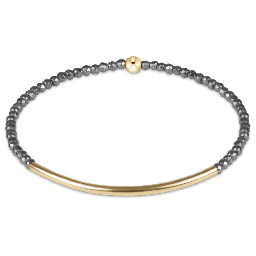 A delicate gold and dark gray beaded bracelet with a curved gold bar, displayed on a clean white background.