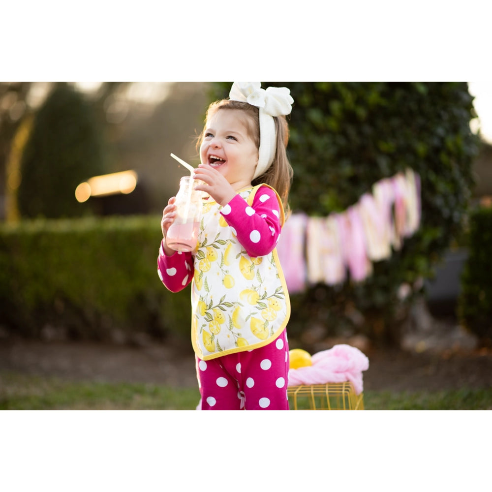 Child in a colorful outfit holding a drink with a straw outdoors.