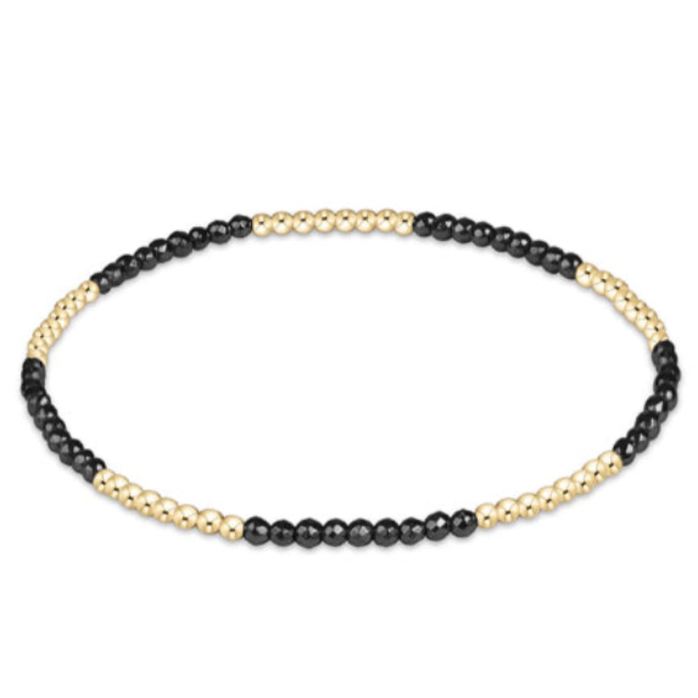 A delicate beaded stretch bracelet featuring alternating sections of small black beads and a gold-toned textured chain, shown on a plain white background.