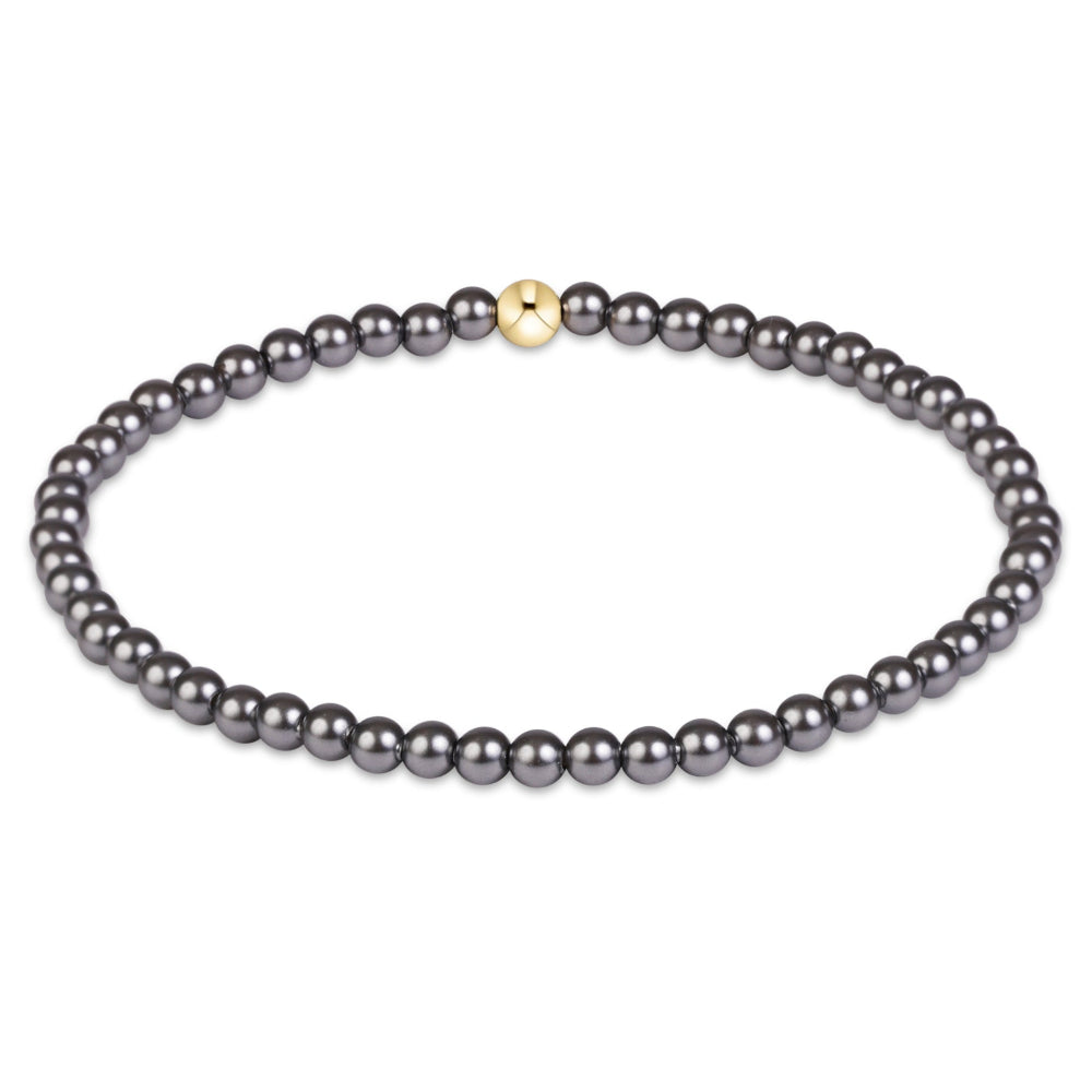 A single-strand beaded bracelet featuring dark gray pearls and a small gold accent bead, displayed on a clean white background.