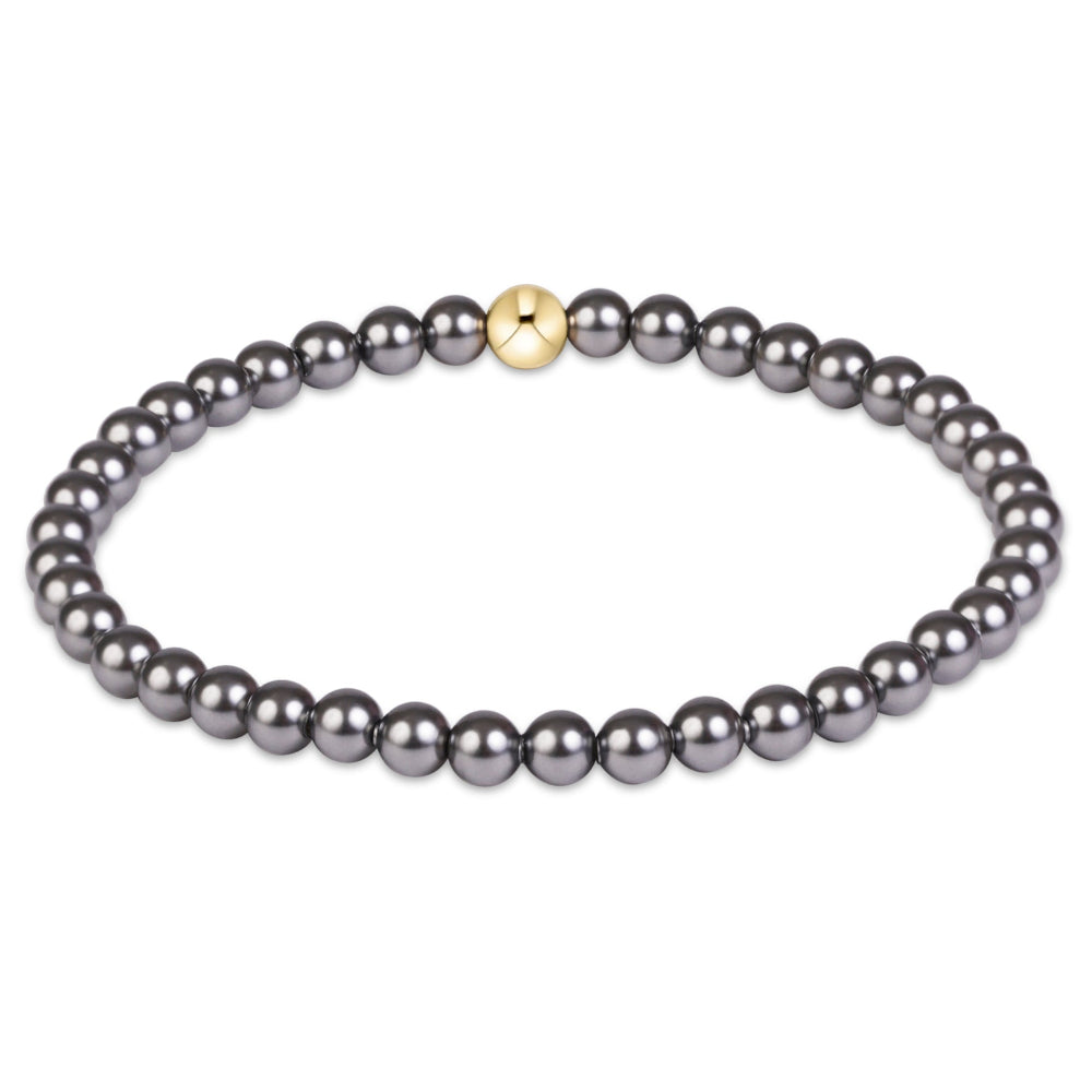A beaded stretch bracelet featuring small, dark gray pearls with a single small gold bead accent at the center, shown on a plain white background.