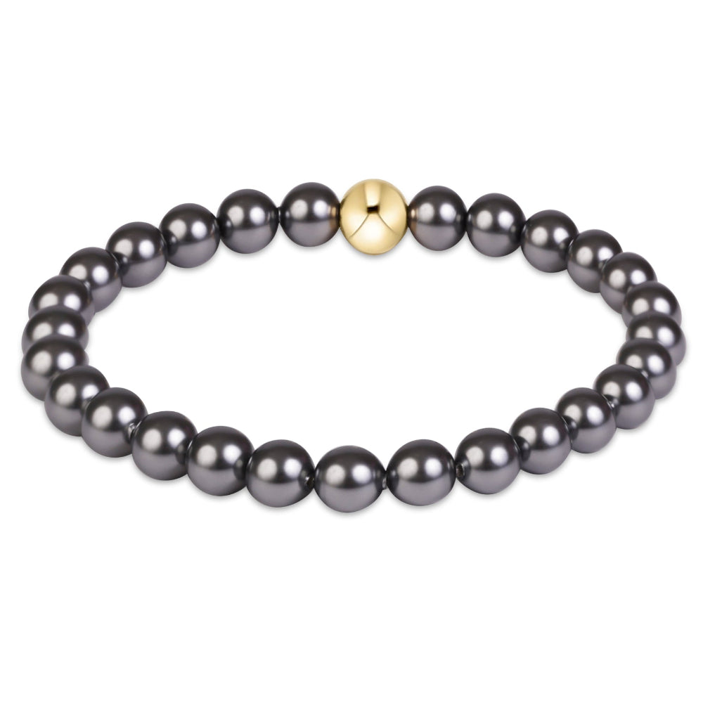 A beaded stretch bracelet featuring dark gray pearls and a central gold-plated round bead , shown on a plain white background.