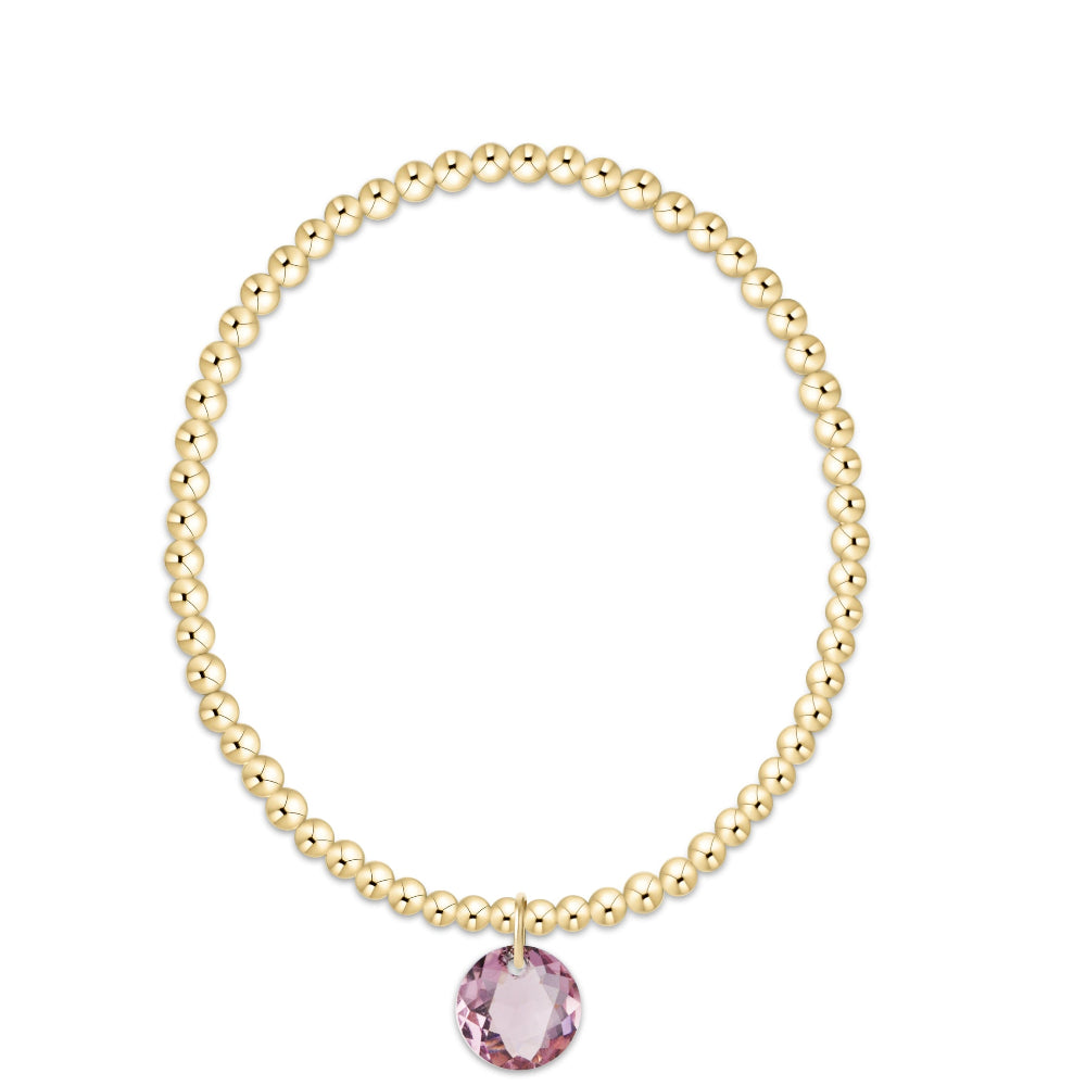 A gold beaded bracelet with a single faceted pink gemstone pendant, displayed on a clean white background.