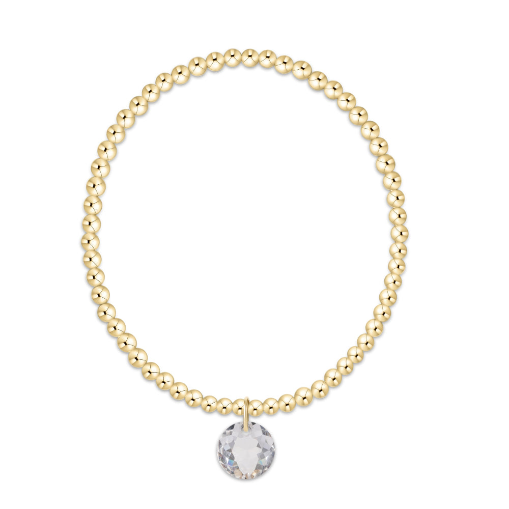 A gold beaded bracelet with a faceted clear crystal charm, displayed on a solid white background.