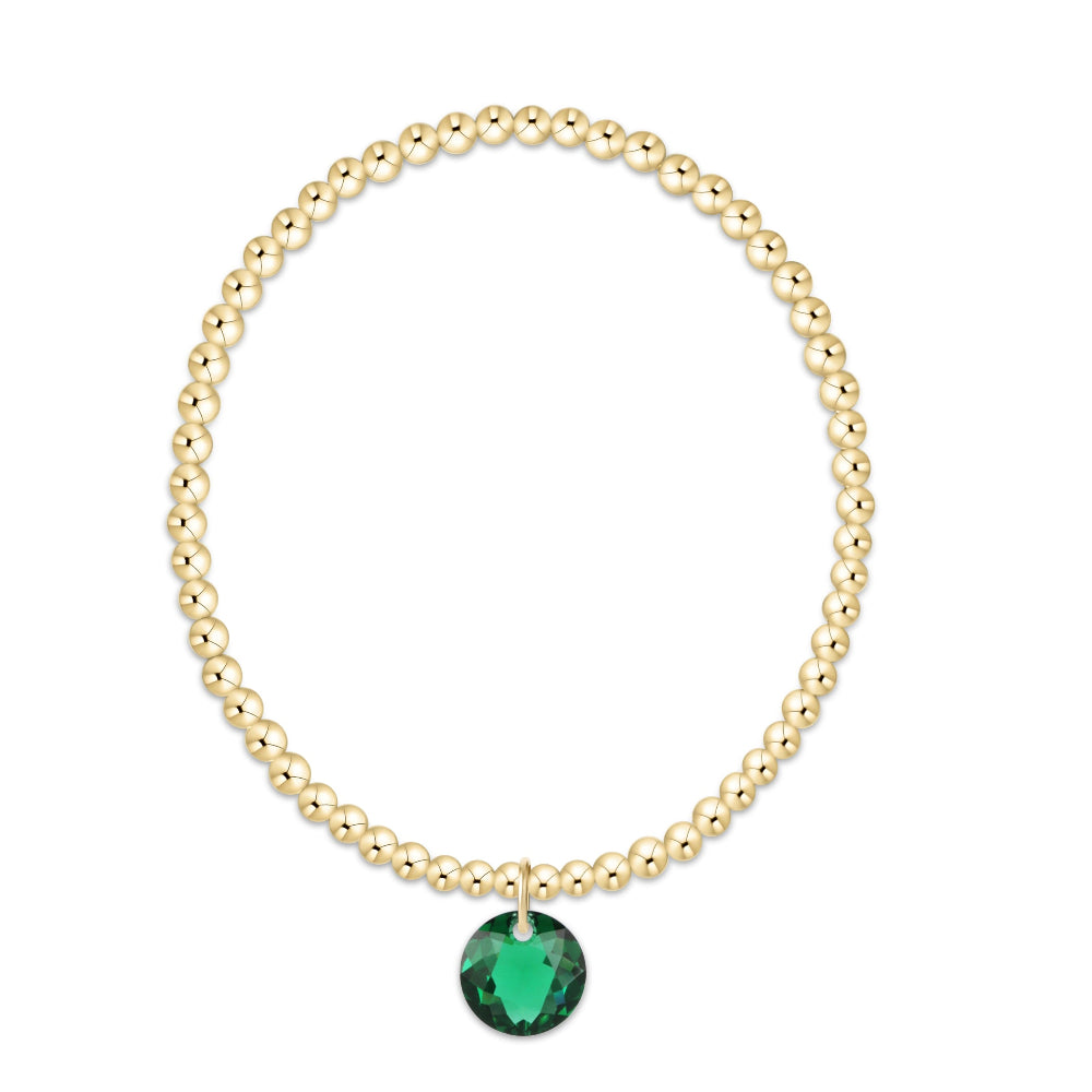 A gold beaded bracelet with a faceted green heart-shaped crystal pendant, displayed on a clean white background.