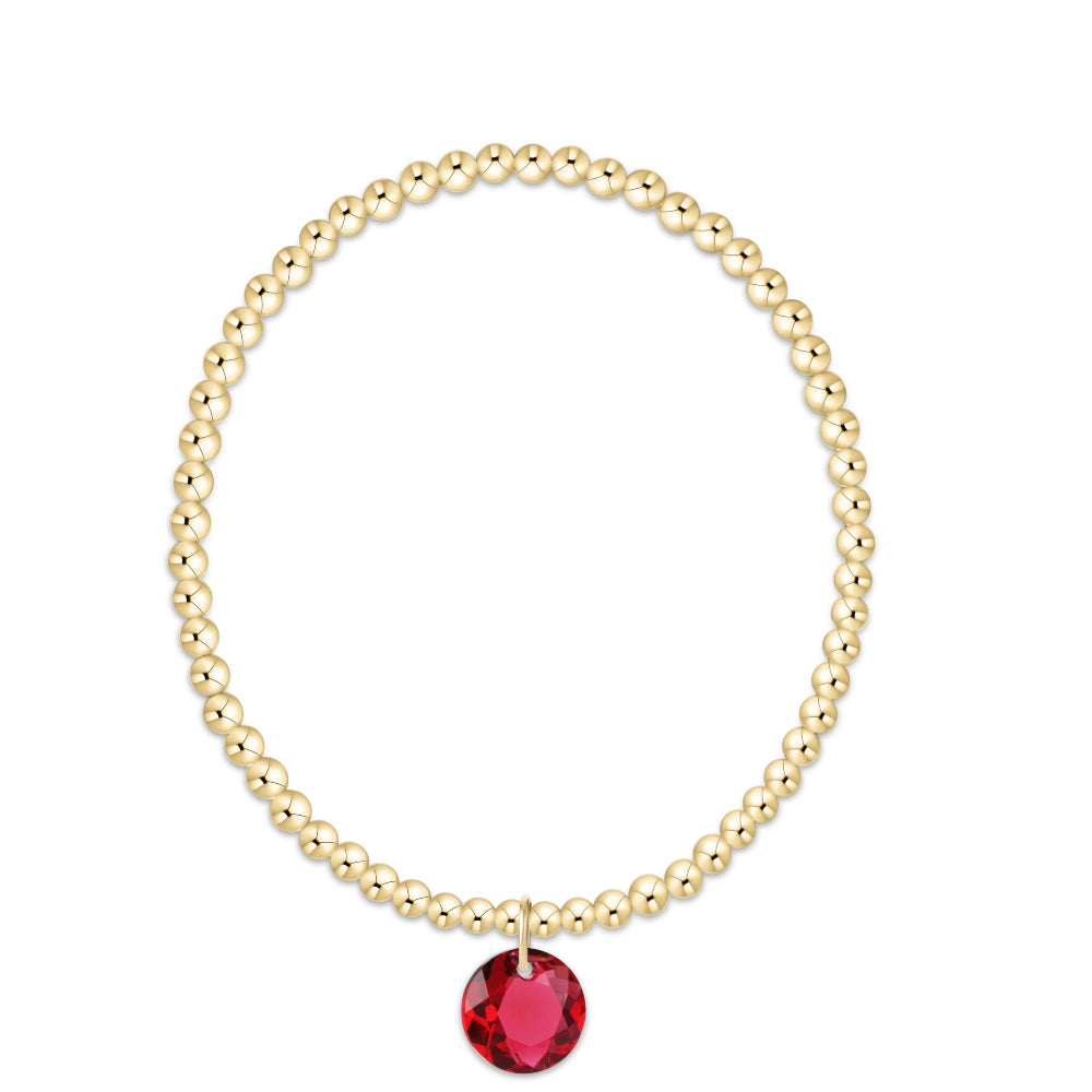 A gold beaded bracelet with a single faceted red gemstone pendant, displayed on a clean white background.