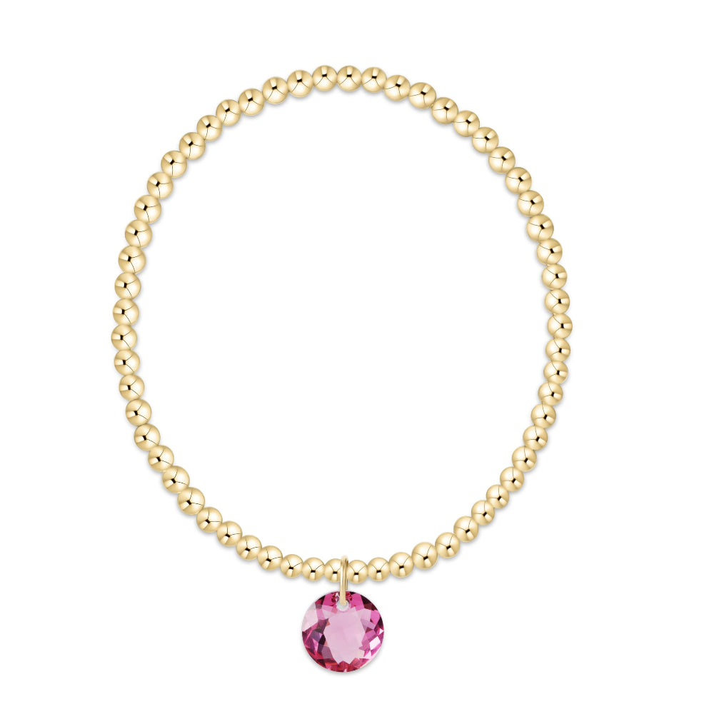 A gold beaded bracelet with a faceted pink gemstone pendant, displayed on a clean white background.