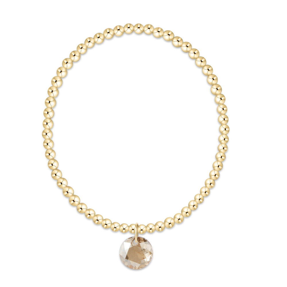 A gold beaded bracelet with a faceted round clear crystal charm, displayed on a clean white background.