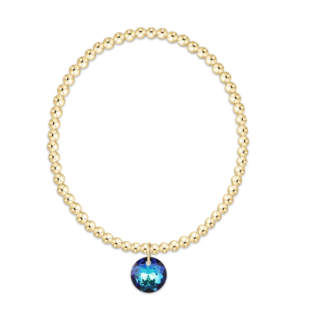 A gold beaded stretch bracelet with a faceted blue gemstone pendant, shown on a plain white background.