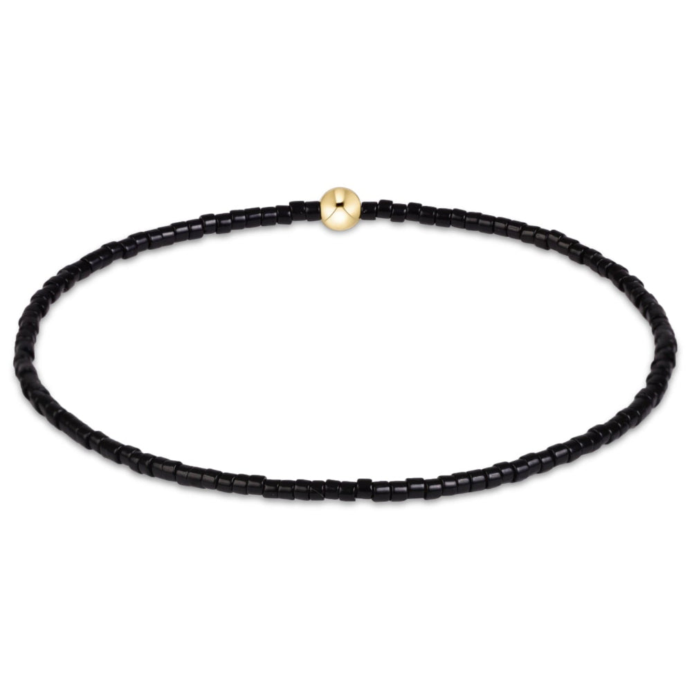 A delicate black beaded bracelet with a single polished gold bead accent at the top, displayed on a clean white background.