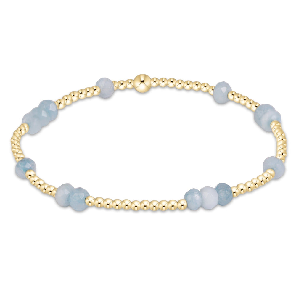 A delicate beaded bracelet featuring alternating strands of polished gold-tone beads and faceted light blue gemstone beads, shown on a plain white background.